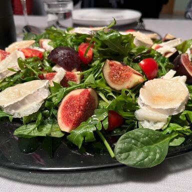 Vegetarischer Salat mit Rucola, Spinat, Ziegenkäse und Feigen auf einem dunklen, gläsernen Teller.