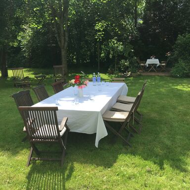 ein mit weißer Tischdecke gedeckter Tisch mit 8 Stühlen und Blumen auf dem Tisch im garten bei Sonnenschein
