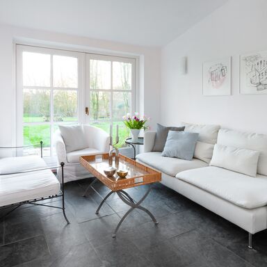 Wintergarten Heller Wintergarten mit weißen Sofas und Sesseln, einem Rattantisch in der Mitte und einem Fenster mit Blick in den Garten