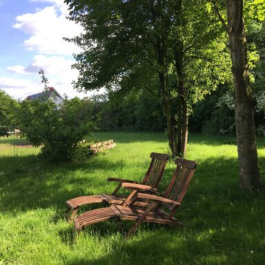 Zwei Liegestühle aus Holz stehen im Halbschatten im Garten