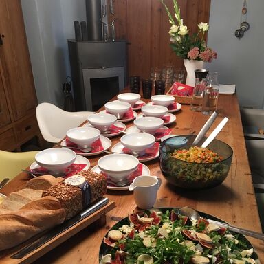 Zwei Schüsseln mit vegetarischen Salaten und diverse Brote stehen vorbereitet auf dem Tisch, dahinter Geschirr und Besteck