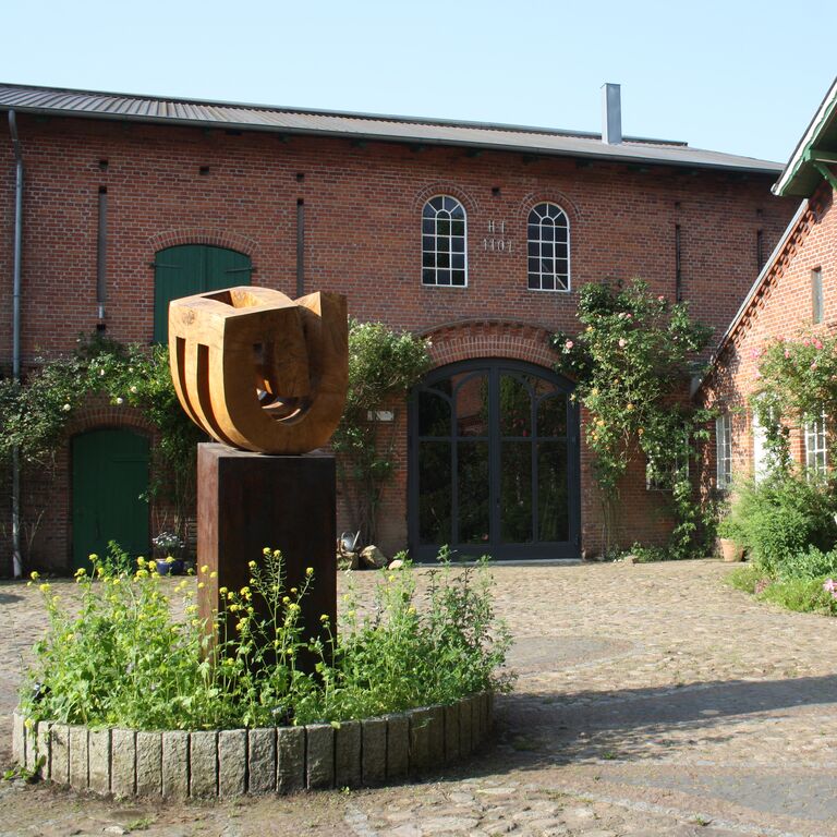 Der Hof Skulptur mit Bepflanzung am Sockel auf dem Hof vor dem Tor zur Diele