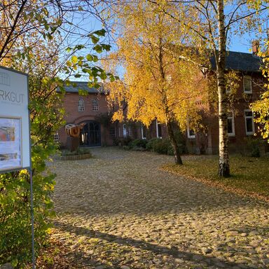 Hof im Herbst Links eine Tafel mit der Aufschrift Werkgut und einem Plakat und Sicht auf die Einfahrt des Werkguts mit herbstlichen Bäumen