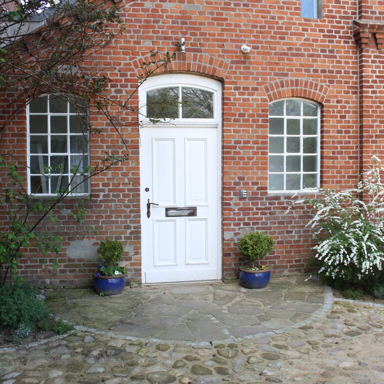 Eine weiße Tür im Backsteingebäude des Werkguts mit zwei blauen bepflanzten Blumentöpfen links und rechts davon