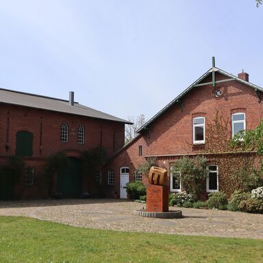 Gutshof mit einem Stück Rasen im Vordergrund, links sieht man den alten Stall mit Diele und Werkstatt, rechts das Haupthaus mit Loft und Privaträumen