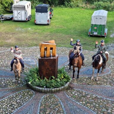 Wanderreiter auf dem Hof Drei Wanderreiter stehen auf dem Hof des Werkgut neben der Skulptur und winken in die Kamera