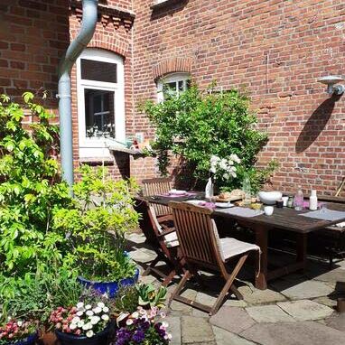 Terrasse am Haupthaus des Werkgut im Sonnenschein mit gedecktem Tisch und Pflanzen in Blumentöpfen im Vordergrund