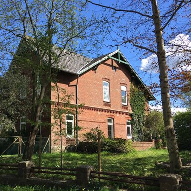 Haupthaus Haupthaus aus roten Backsteinen von der Sonne angestrahlt mit Garten und Bäumen rundherum