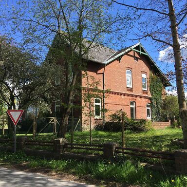 Haupthaus von der Straße aus fotografiert, rundherum Garten und Bäume