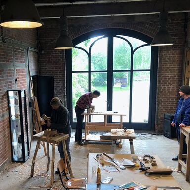 Teilnehmer beim Workshop Holzbildhauen bearbeiten ihre Kunstwerke und der Kursleiter sieht zu