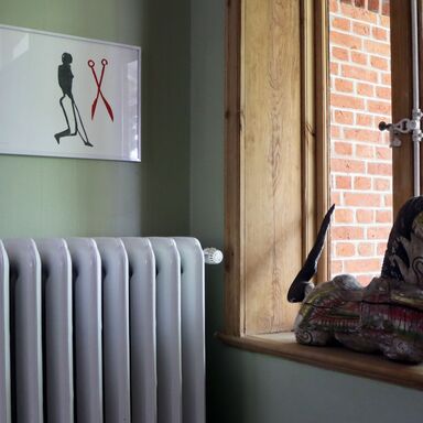 Holzskulptur eines Pferdes auf dem Fensterbrett im Eingangsbereich, über einem Heizkörper hängt ein Bild mit einem Männchen und einer roten Schere