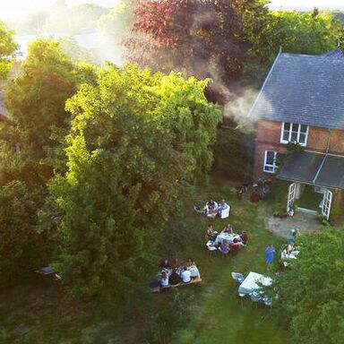 Das Gut von oben Blick auf den sonnigen Garten des Haupthauses von oben, einige gedeckte Tische mit Menschen über die Wiese verteilt
