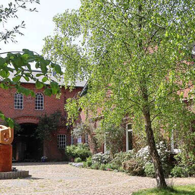 Gutshof mit Skulptur in der Einfahrt, umgeben von Bäumen