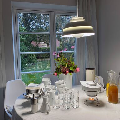 Vorbereites Porzellangeschirr von Mikaela Dörfel auf einem runden Tisch mit weißer Tischdecke, alles ist für die Kaffeepause vorbereitet