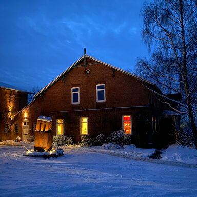 Winterstimmung Gutshof im Schnee, es ist dunkel und die warmen Lichter leuchten aus dem Haus